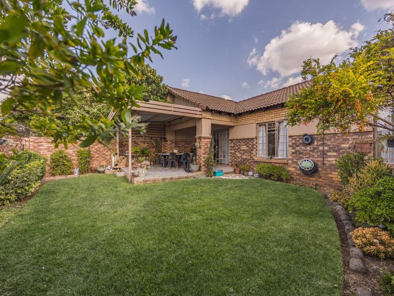 A well-maintained rear garden featuring a lawn, established landscaping, and a covered patio area with a timber pergola structure.