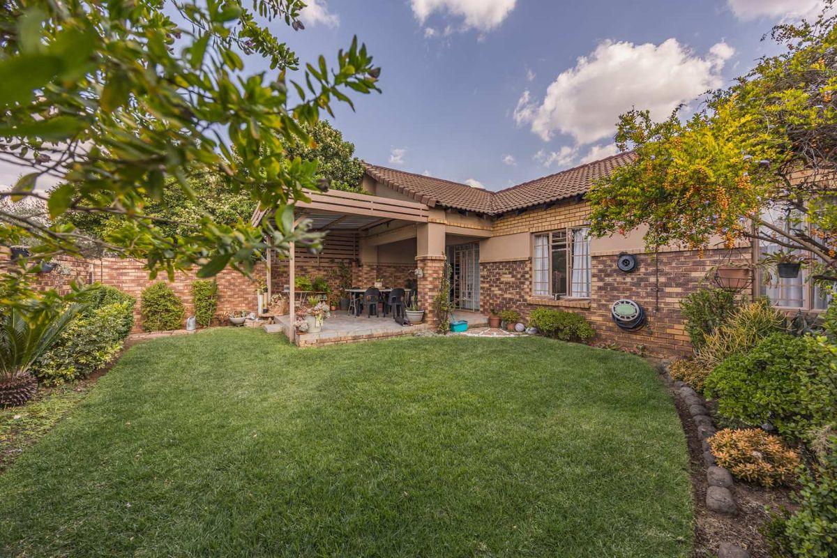 A well-maintained rear garden featuring a lawn, established landscaping, and a covered patio area with a timber pergola structure.