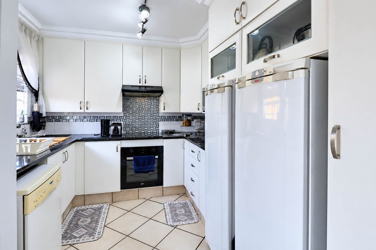 A well-maintained kitchen featuring white cabinetry, granite countertops, a mosaic tile backsplash, and built-in appliances with ceramic floor tiling.