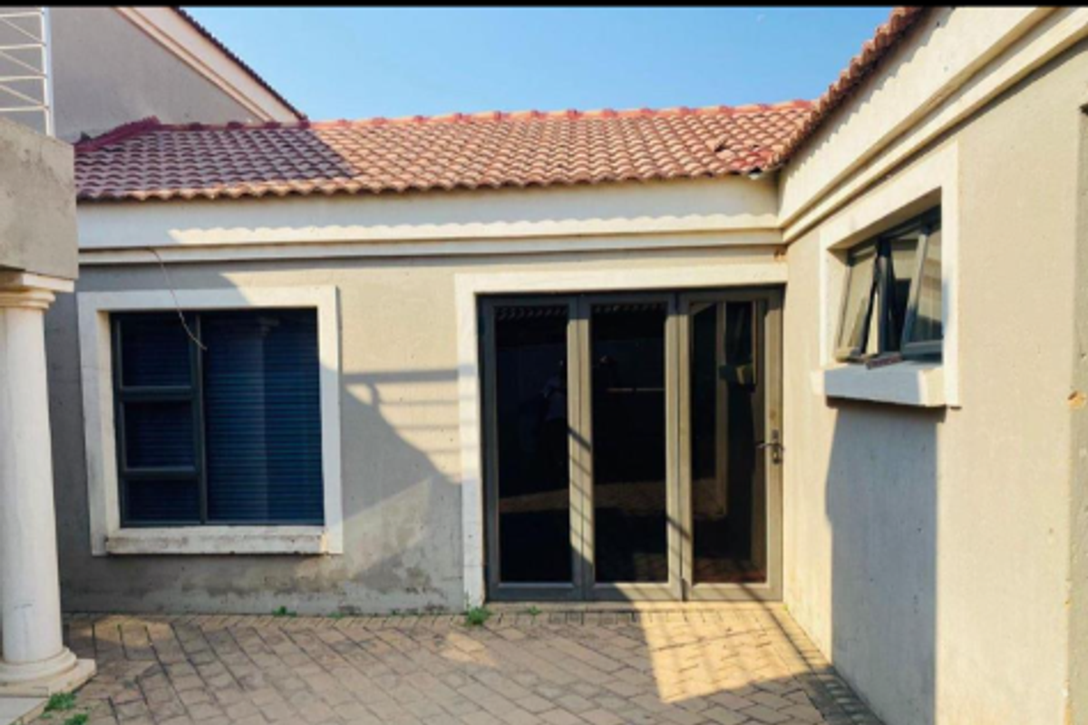Rear exterior view of the property featuring a paved patio area, tiled roof, and dark aluminium framed windows and sliding door.