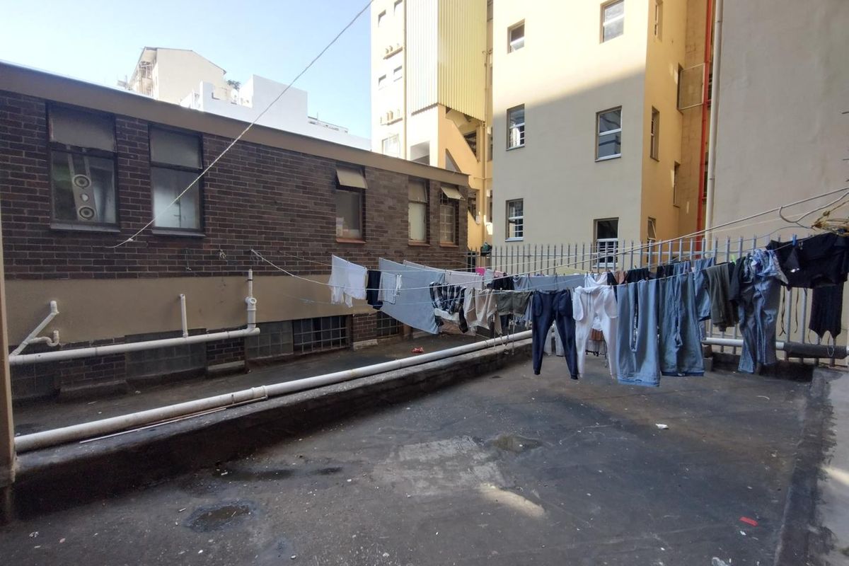 An exterior utility area featuring a concrete surface, perimeter fencing, and exposed building infrastructure, currently utilized for laundry drying.