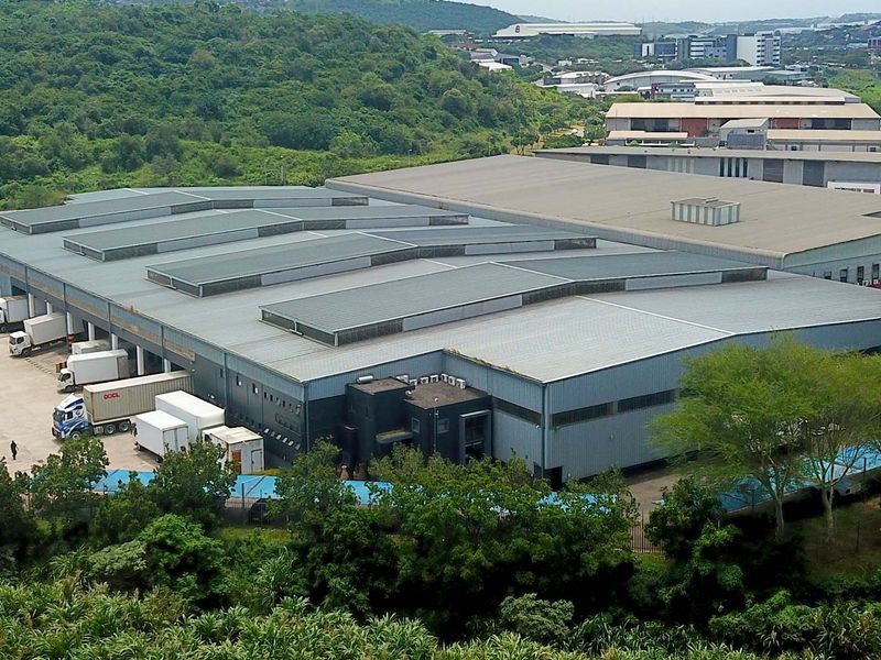 Aerial view of a large industrial warehouse facility featuring extensive metal roofing, loading bays, and a paved yard area within a landscaped estate.