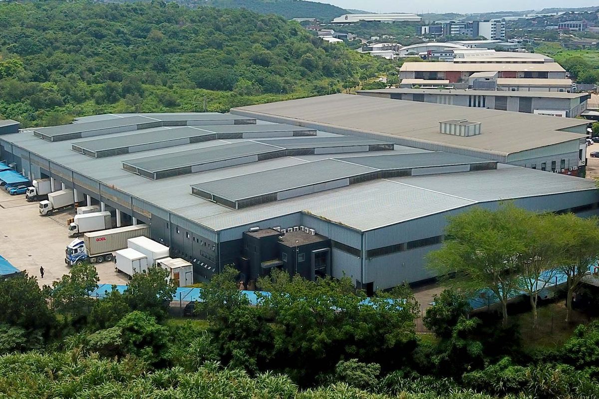 Aerial view of a large industrial warehouse facility featuring extensive metal roofing, loading bays, and a paved yard area within a landscaped estate.