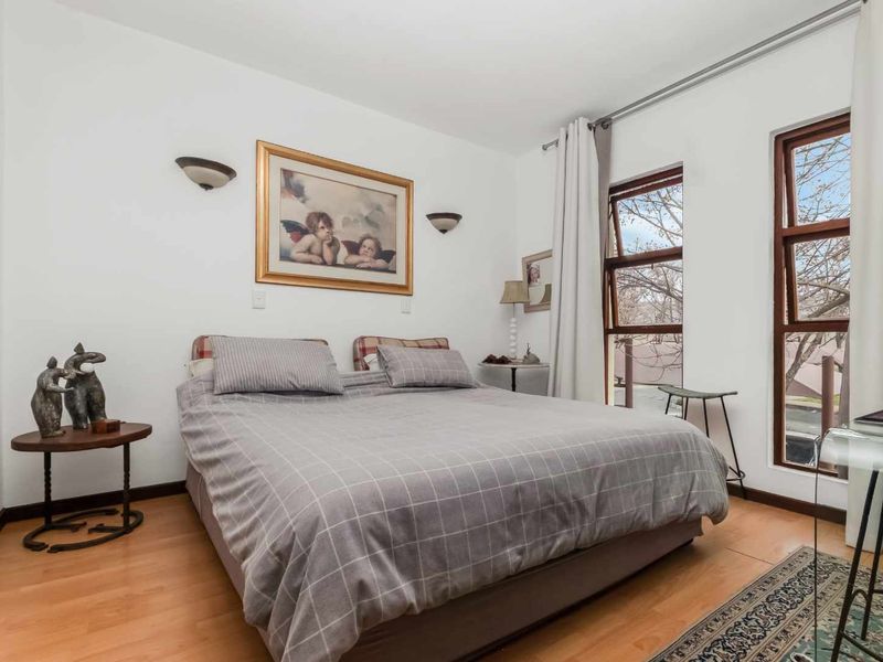 A well-lit bedroom featuring laminate flooring, wall-mounted lighting, and large timber-framed windows that provide natural light.