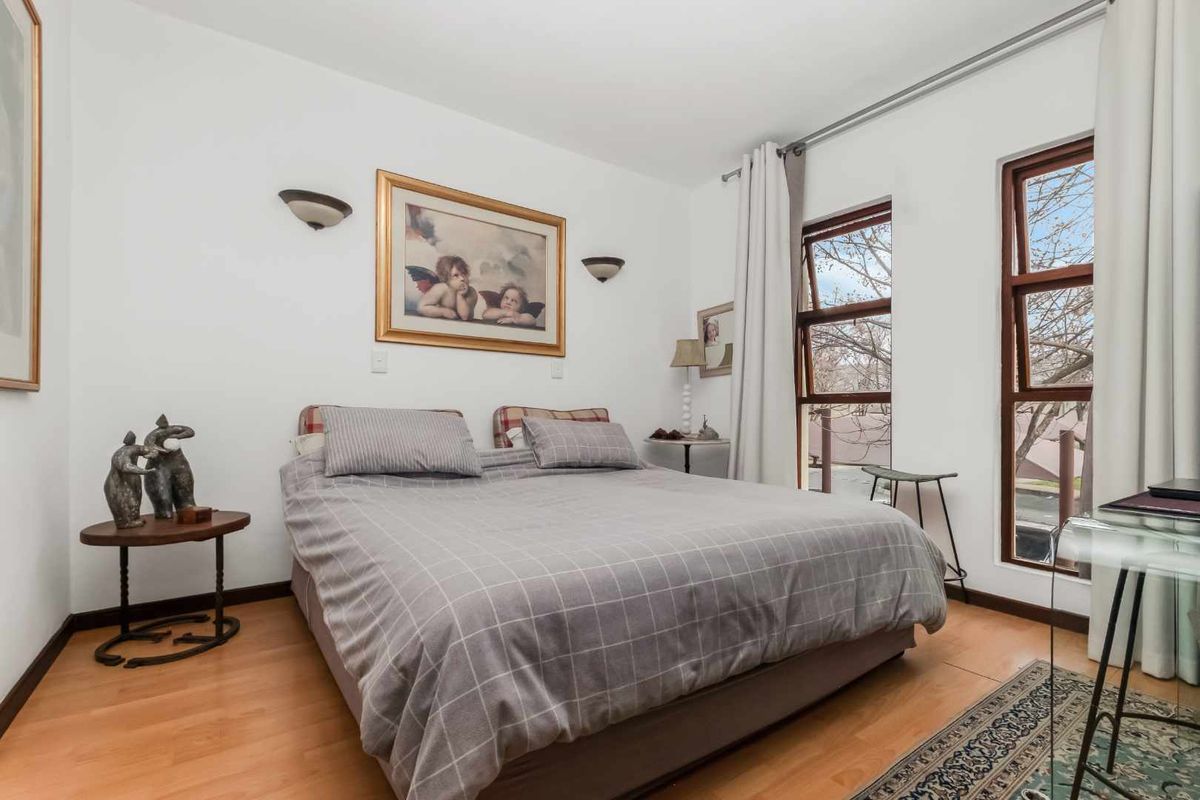 A well-lit bedroom featuring laminate flooring, wall-mounted lighting, and large timber-framed windows that provide natural light.