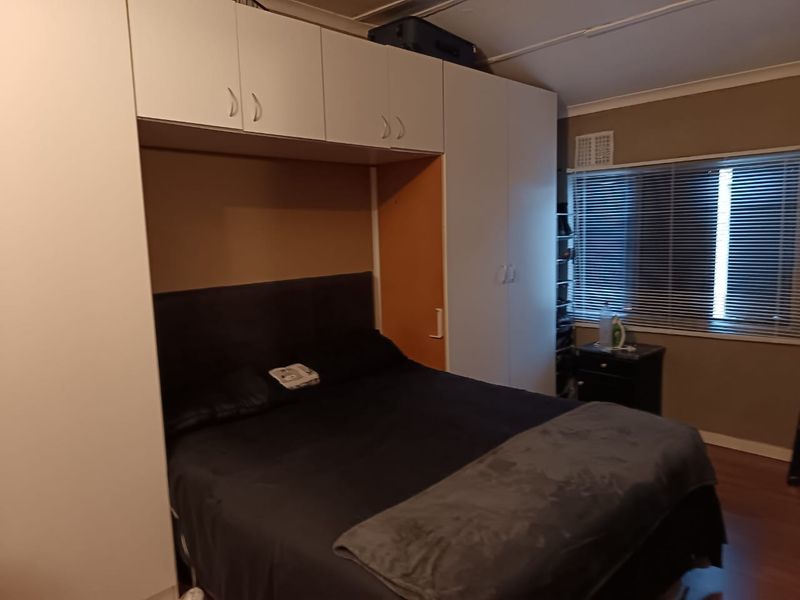 Bedroom featuring extensive built-in wardrobe storage with overhead cabinetry, laminate flooring, and venetian blinds.