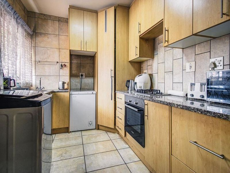Functional kitchen featuring light wood cabinetry, granite countertops, built-in oven, gas hob, and tiled finishes throughout.