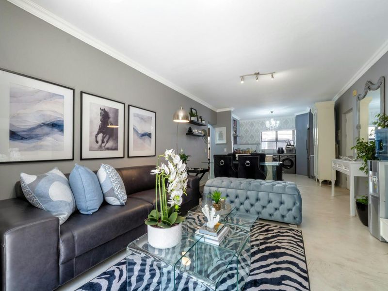 An open-plan living and dining area featuring neutral wall tones, crown molding, tiled flooring, and a connected kitchen space with built-in cabinetry.