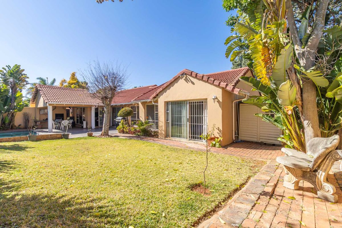 Rear view of the house featuring a tiled roof, sliding glass doors, a covered patio area, and a swimming pool set within a landscaped garden.