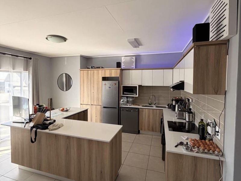 Modern kitchen featuring wood-grain cabinetry, stone countertops, a central island, and integrated appliances with neutral tiled flooring and backsplash.