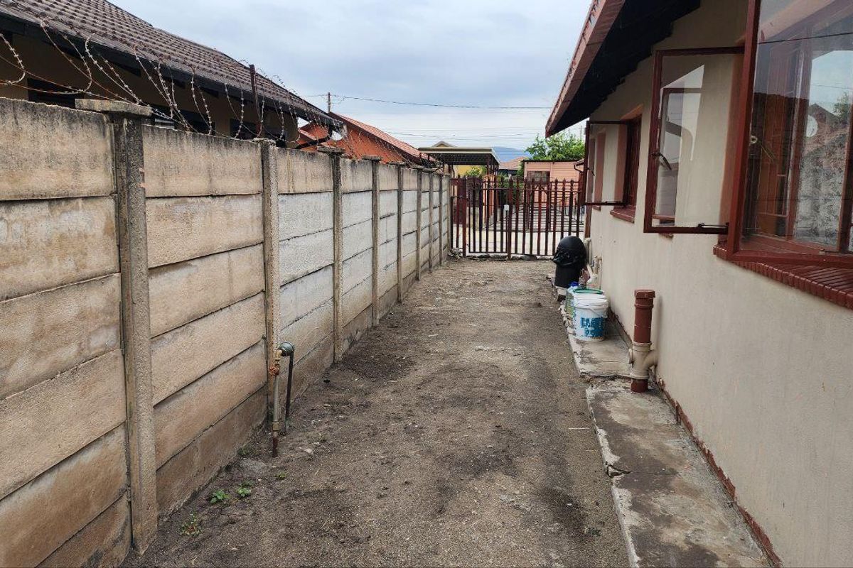 A narrow side exterior passage featuring a precast concrete boundary wall with security wire and direct access to the rear property gate.