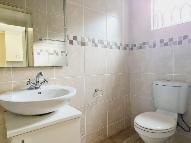 A clean, well-maintained bathroom featuring neutral ceramic wall and floor tiles, a modern vessel sink on a vanity cabinet, and a wall-mounted mirror.