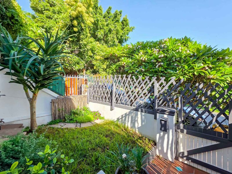 A well-maintained private garden area featuring established greenery, a secure boundary wall with lattice fencing, and a pedestrian gate entrance.
