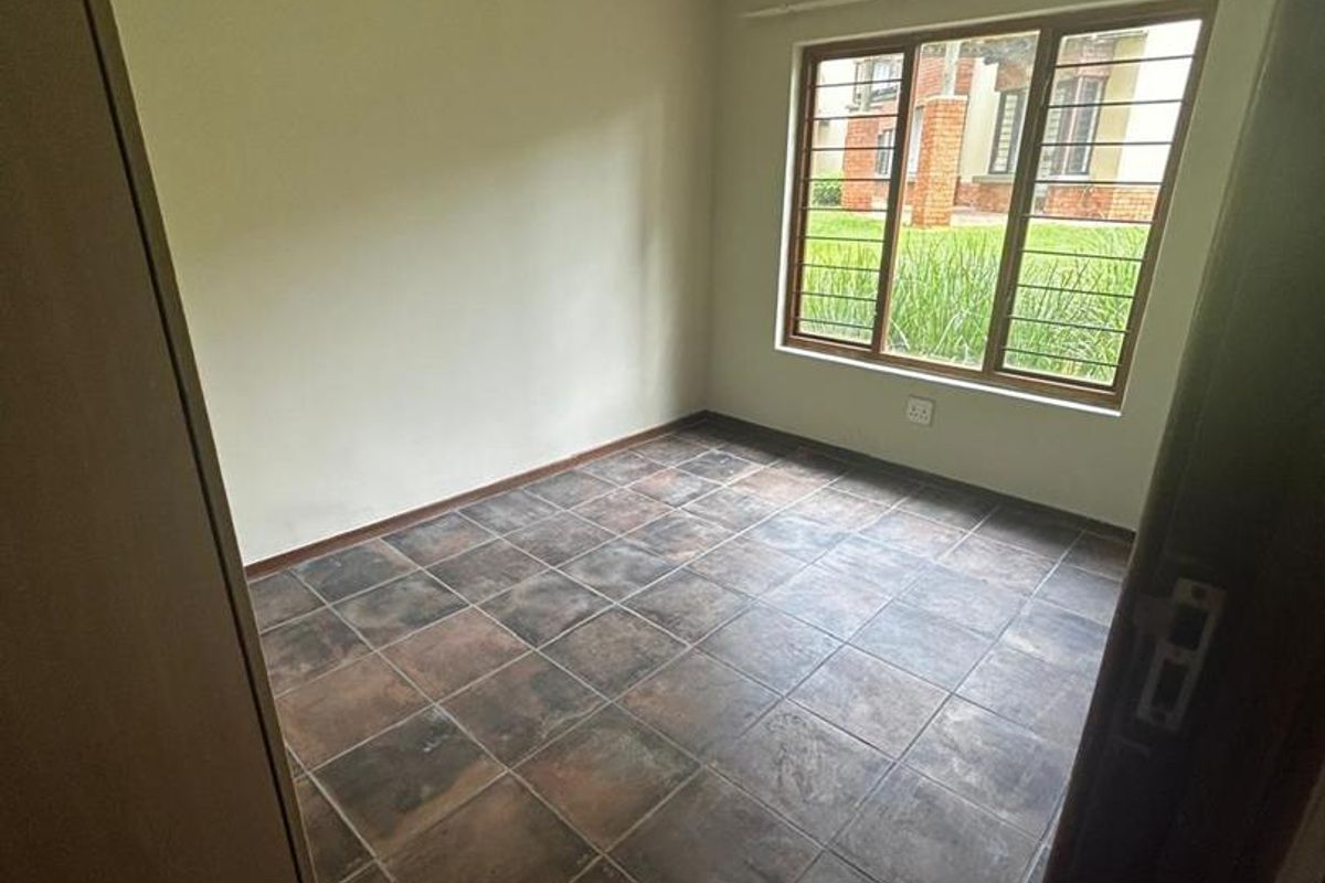 A vacant bedroom featuring dark ceramic floor tiles, a large window with security bars, and neutral wall finishes.