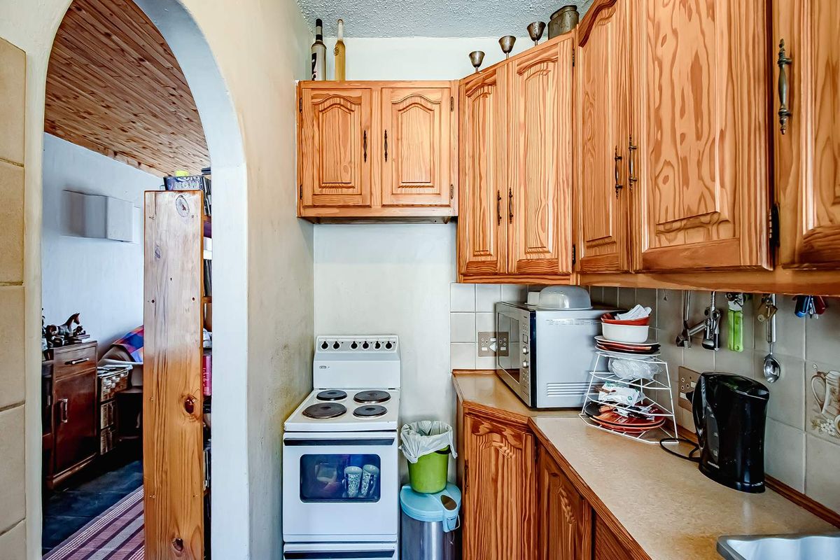 A compact kitchen featuring traditional wood cabinetry, a freestanding electric stove, and tiled backsplash, accessible through a classic arched doorway.