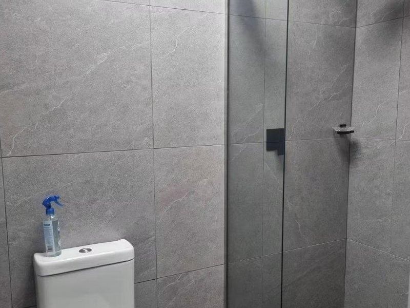 Modern bathroom featuring a walk-in shower with a rain shower head, glass screen, and contemporary grey wall tiling with a black tiled shower floor.