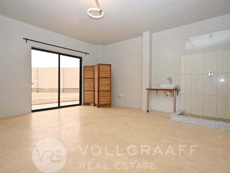 Spacious bedroom featuring polished concrete floors, a sliding door to the exterior, and an open-plan en-suite bathroom with a walk-in shower.