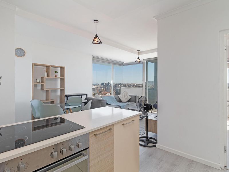 Modern open-plan apartment featuring a functional kitchen with built-in oven and hob, flowing into a bright living area with expansive city views.