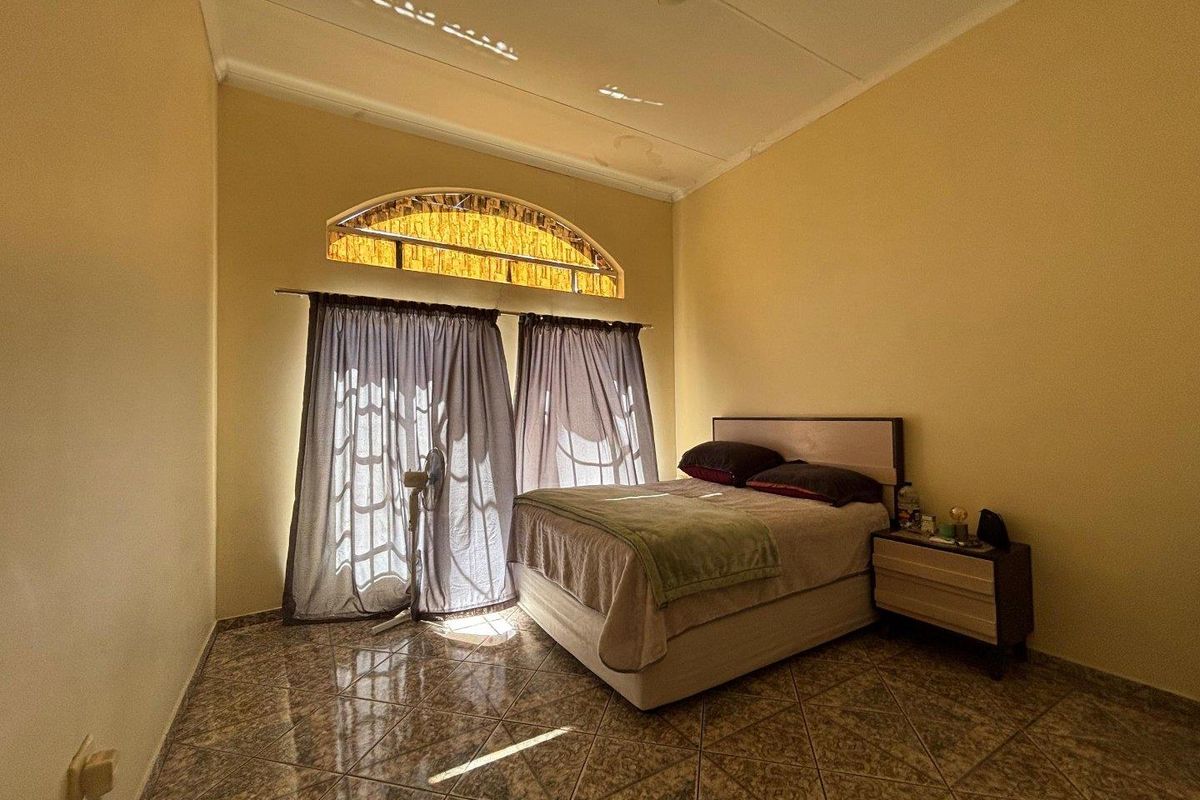A bedroom featuring tiled flooring, a distinctive arched window with decorative glass, and neutral wall finishes.