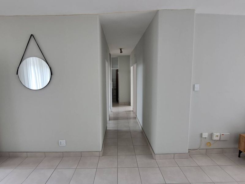 A clean, neutral-toned hallway featuring tiled flooring and simple architectural lines, providing access to other areas of the apartment.