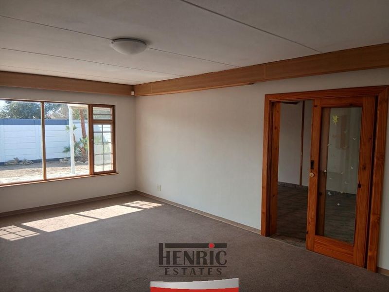 A spacious, empty living room featuring neutral carpeting, a large window, and a distinctive timber-framed sliding door leading to an adjacent area.