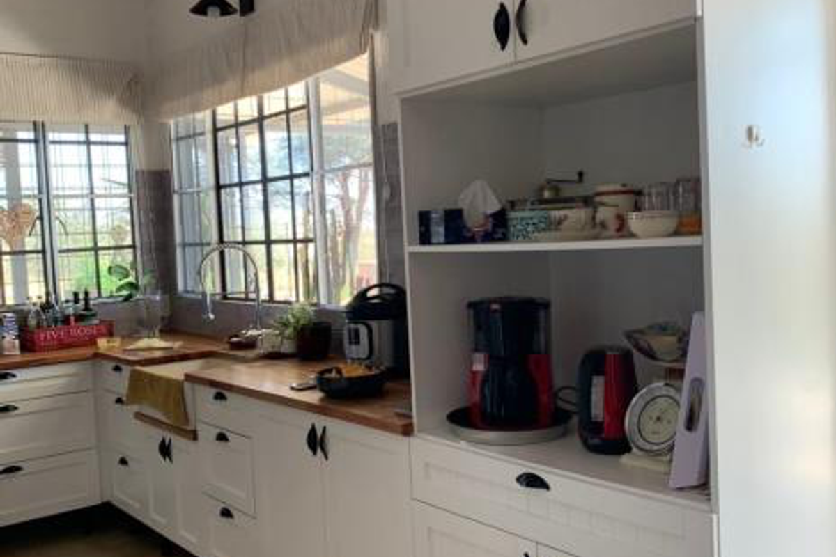 A bright kitchen featuring white cabinetry, wooden countertops, a farmhouse-style sink, and large windows with grid detailing, offering a clean and functional workspace.