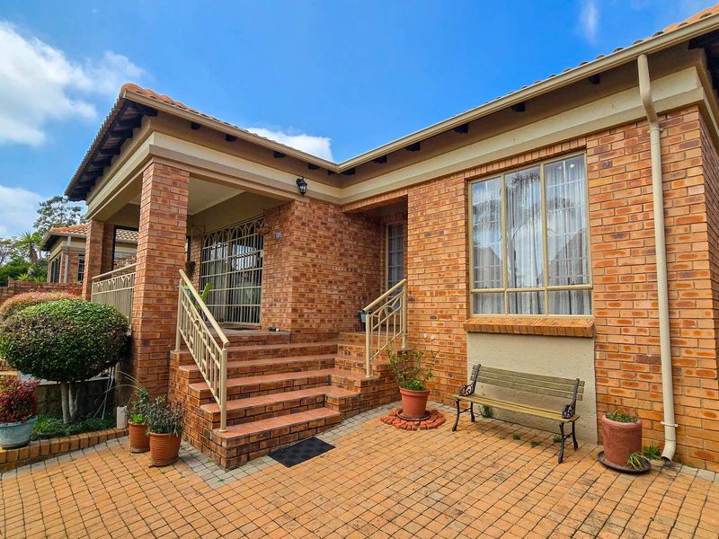 Rear view of a face brick townhouse featuring a covered patio, brick paved courtyard, and secure access points.