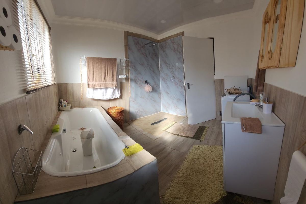 A functional bathroom featuring a built-in bathtub, a walk-in shower with marble-look wall panels, and a vanity unit with a basin.