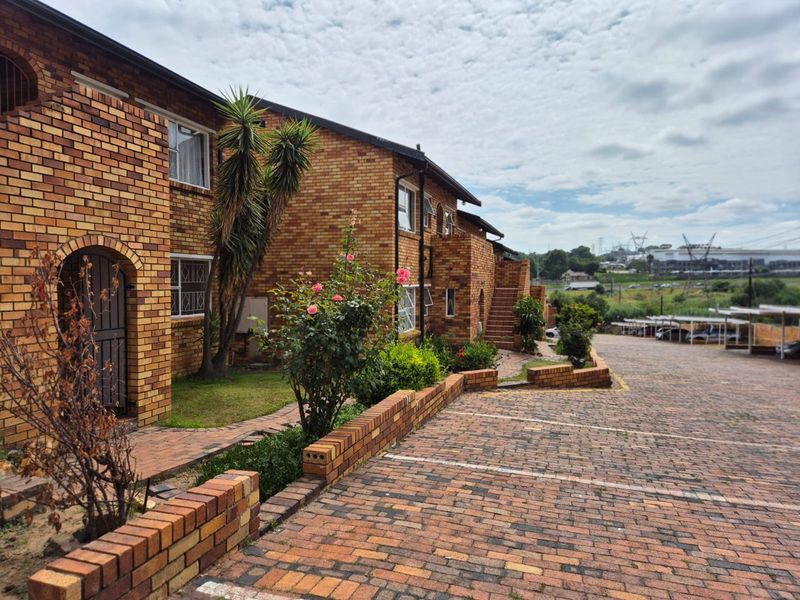 Exterior view of a face brick apartment complex featuring a paved driveway, landscaped garden areas, and secure access points.