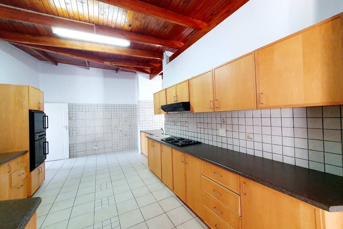 Spacious kitchen featuring wooden cabinetry, dark countertops, a built-in oven, gas hob, extractor fan, and exposed timber ceiling beams.