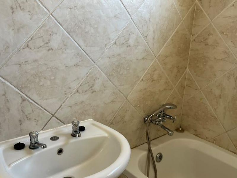 A functional bathroom featuring a pedestal basin, bathtub with handheld shower mixer, and neutral diamond-patterned wall tiling.