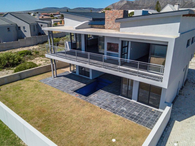 Aerial view of a modern double-story house featuring a rear balcony, built-in fireplace, tiled patio, and a swimming pool set within a fenced garden.