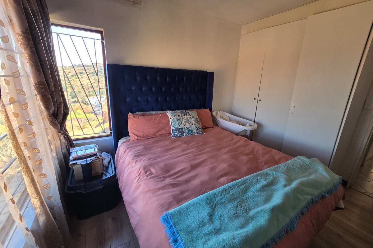 A bedroom featuring built-in cupboards, laminate flooring, and security bars on the window, offering a functional space with potential for cosmetic updates.
