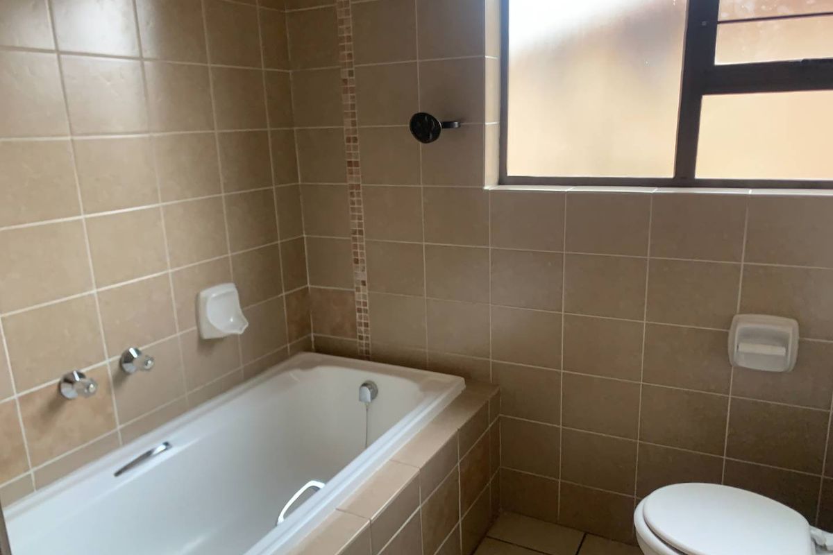 A functional bathroom featuring a built-in bathtub with wall-mounted mixer, tiled surround, and a standard toilet.