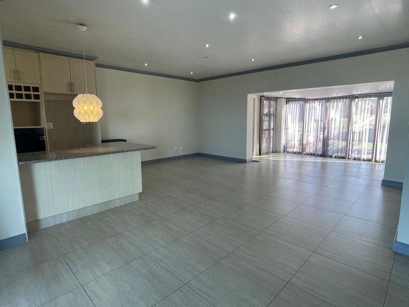 Spacious open-plan living area featuring tiled floors, recessed lighting, and a kitchen with granite countertops, leading to a bright rear patio through sliding doors.