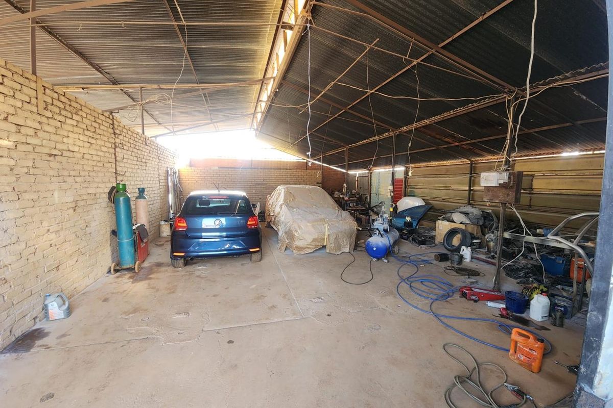 A large, industrial-style workshop or garage space featuring exposed brick walls, a corrugated metal roof, and concrete flooring, currently used for vehicle maintenance.