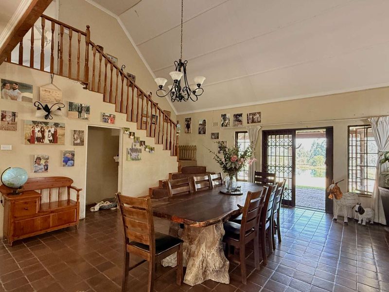 Spacious open-plan dining area featuring vaulted ceilings, tiled flooring, and a wooden staircase, with direct access to the outdoor patio through sliding glass doors.