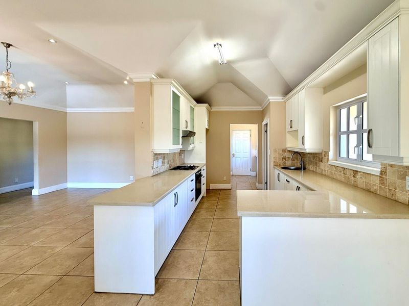 Spacious open-plan kitchen featuring white cabinetry, stone countertops, integrated appliances, and tiled flooring, flowing seamlessly into the adjacent living area.