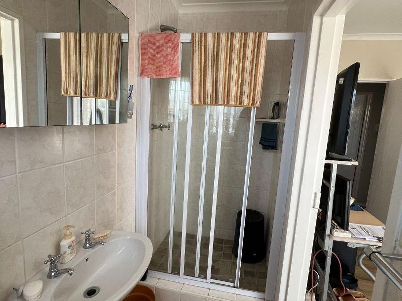 A functional bathroom featuring a pedestal basin, tiled walls, and a shower enclosure with a white frame.