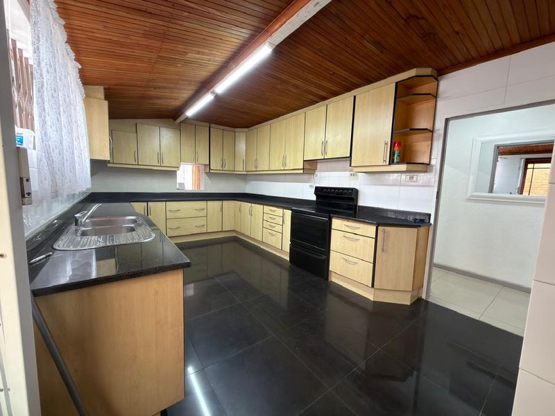 Spacious kitchen featuring light wood cabinetry, dark granite countertops, black tiled flooring, and a distinctive timber ceiling.
