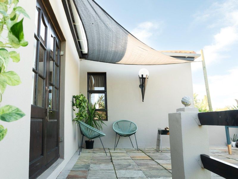 A well-maintained outdoor patio featuring stone paving, a protective shade sail, and direct access to the interior through timber-framed glass doors.