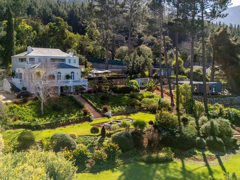 Aerial view of a multi-level residence set within a lush, landscaped garden featuring stone retaining walls, a central water feature, and mature trees.