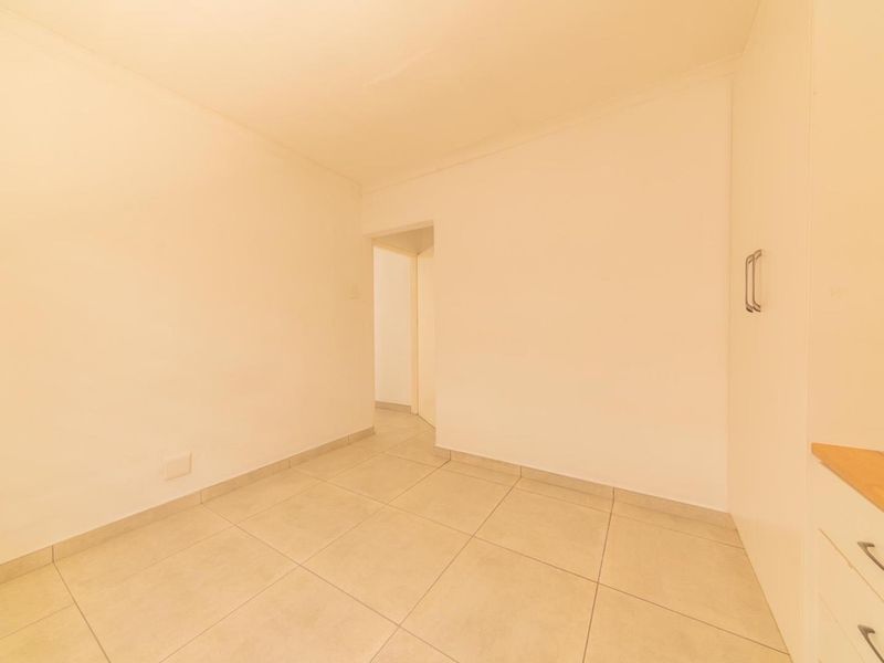 A bright, empty bedroom featuring neutral tiled flooring and built-in cupboards, offering a clean and versatile space ready for personalization.