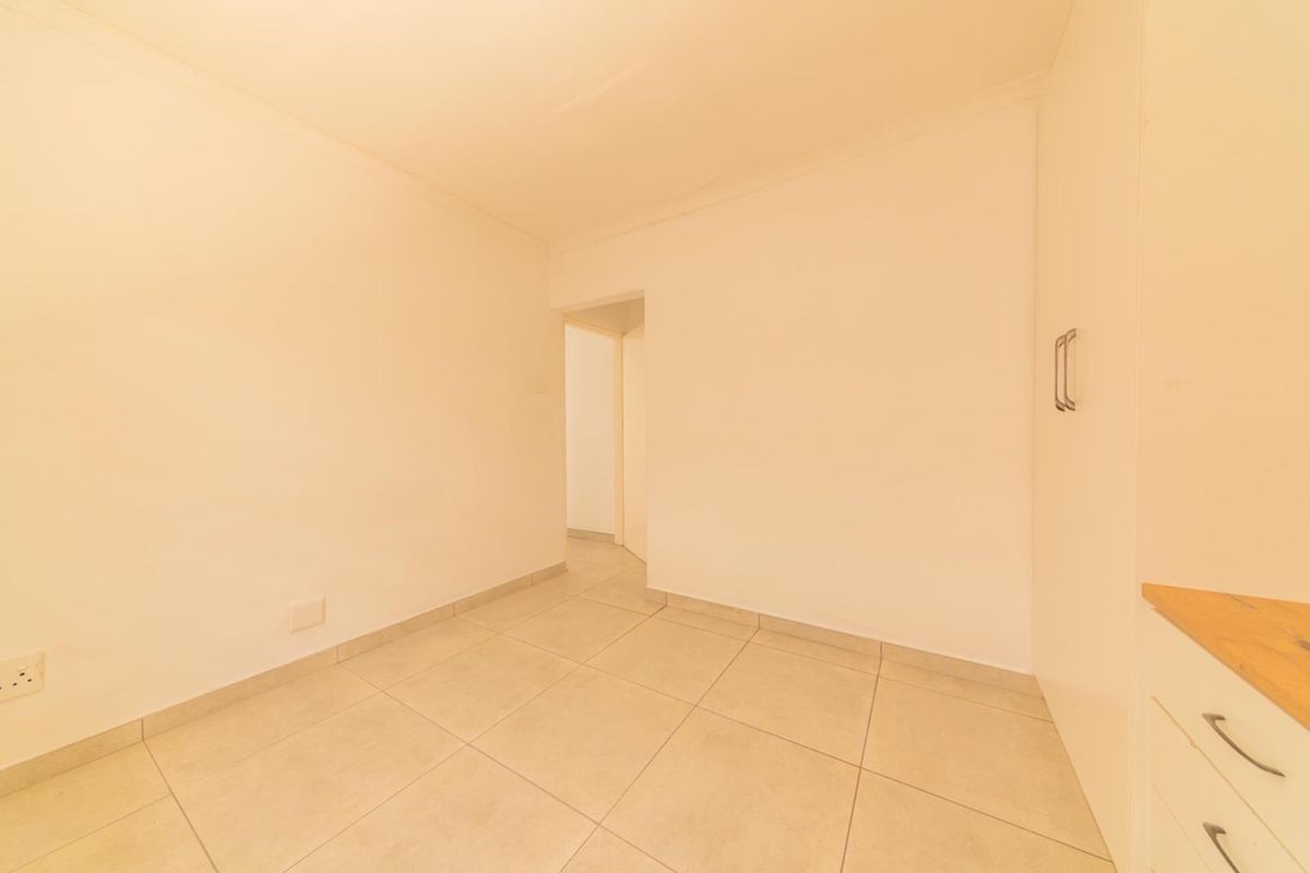 A bright, empty bedroom featuring neutral tiled flooring and built-in cupboards, offering a clean and versatile space ready for personalization.