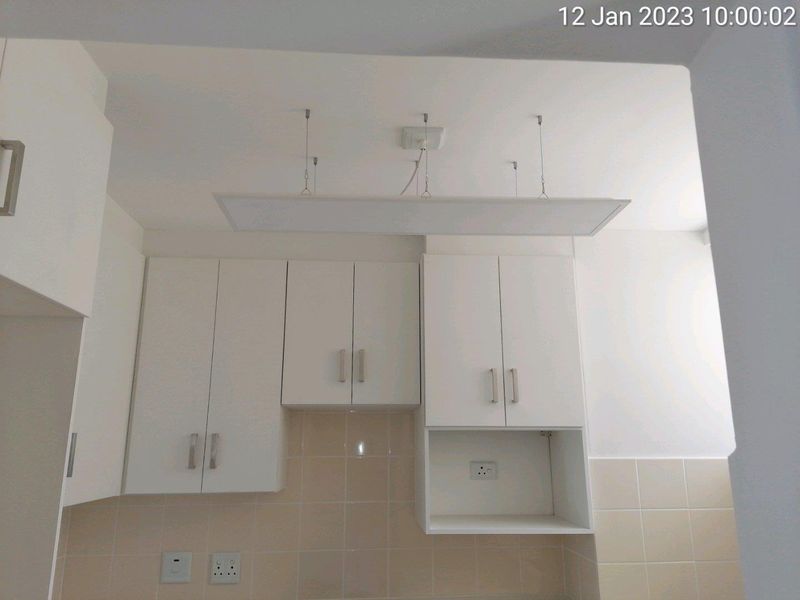 A clean kitchen area featuring white cabinetry, a neutral tiled backsplash, and a modern suspended light fixture.