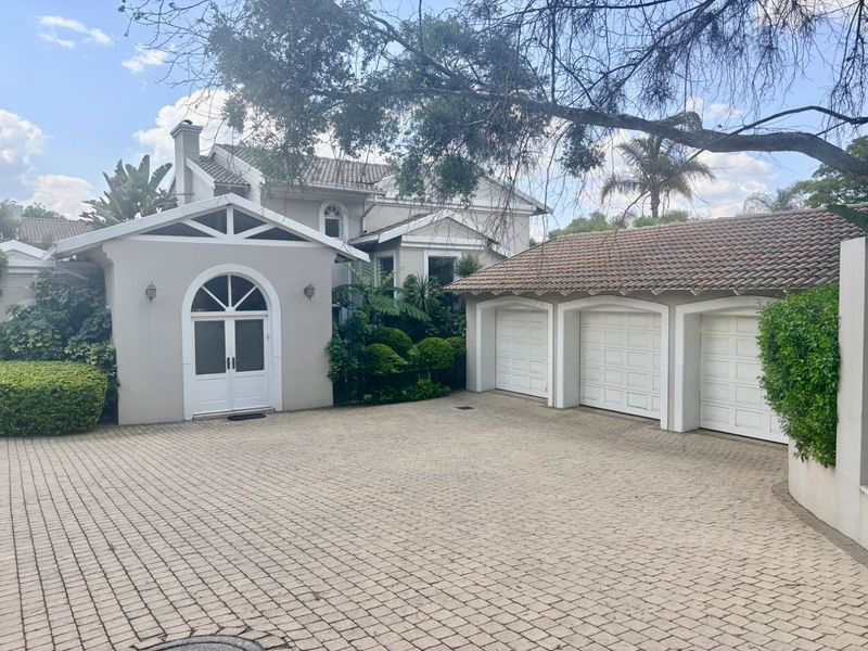 A well-maintained front exterior featuring a spacious paved driveway, a triple garage, and an elegant arched double door entrance.