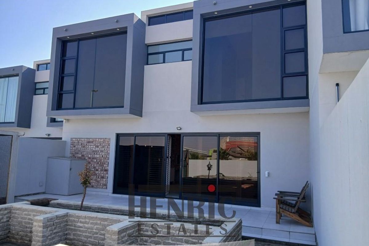Modern rear elevation of an apartment featuring large sliding glass doors, contemporary aluminium window frames, and a paved patio area.