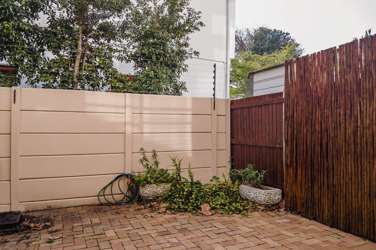 A private outdoor courtyard featuring paved flooring, a precast concrete boundary wall, and timber privacy screening with electric fencing.