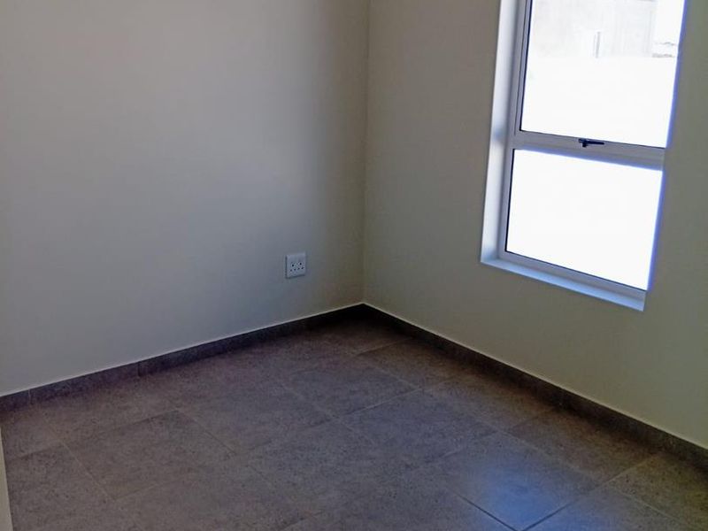 A clean, empty bedroom featuring neutral wall paint, tiled flooring, and a modern aluminium window frame, providing a blank canvas for interior design.