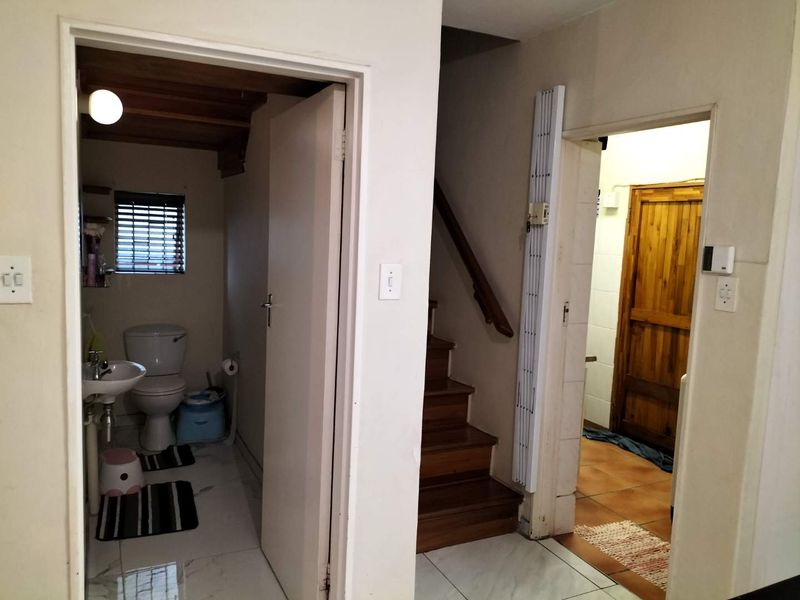 Interior view showing a hallway with a staircase, access to a bathroom, and a secondary room with wooden door.